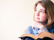 a young woman reading a Bible and looking up to God 