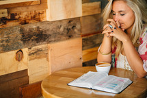 A young woman in prayer, with an open Bible and cup of coffee.