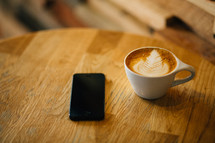 A cup of coffee and a cell phone on a table.