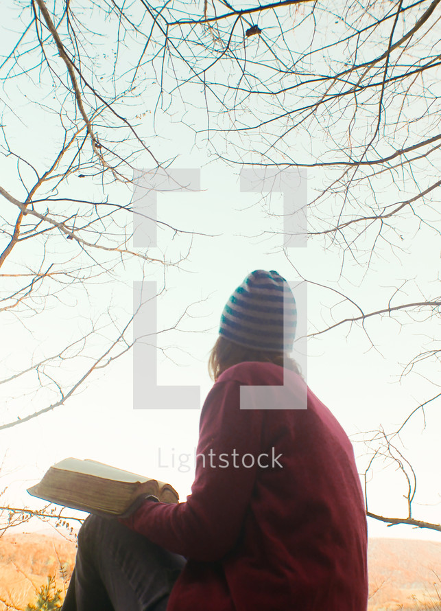 a woman reading a Bible outdoors by a lake in fall 