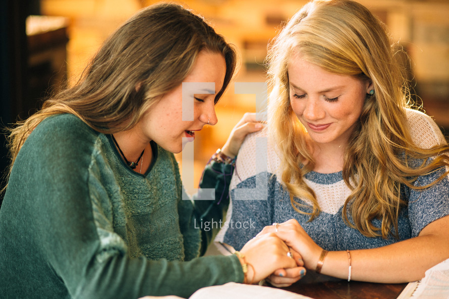 Two women embracing during prayer at a table with Bibles.