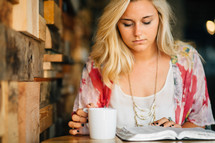 A young woman reads the Bible with a cup of coffee.