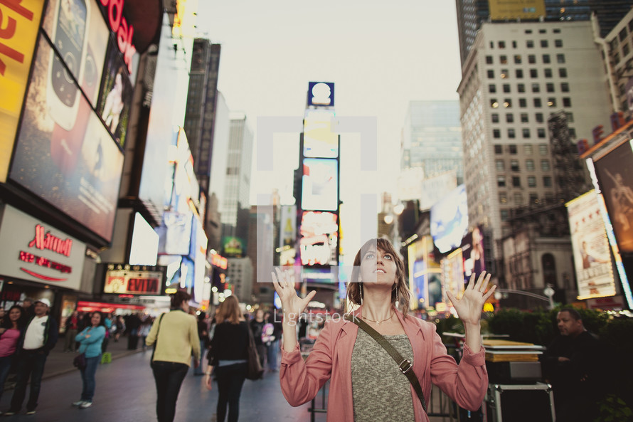 a young white woman with her hands raised in the middle of Time Square