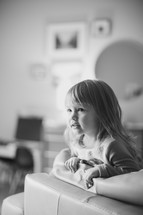 a toddler girl looking over a couch 
