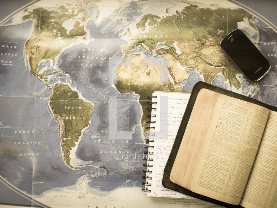 open Bible, journal, and cellphone on a map 