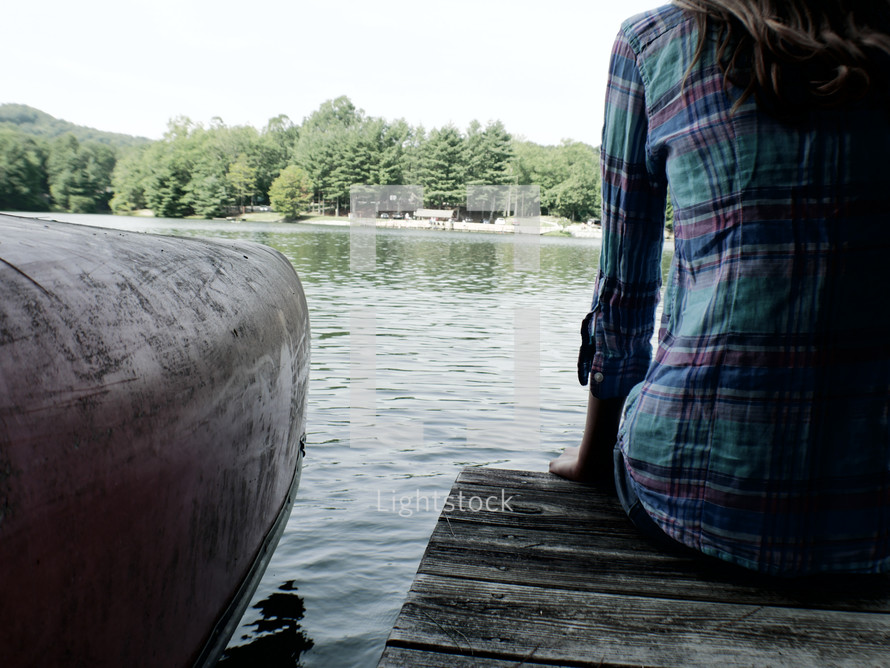 teen girl sitting on a pier on a lake beside a canoe 