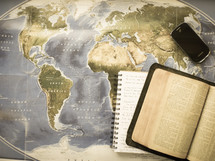 open Bible, journal, and cellphone on a map 