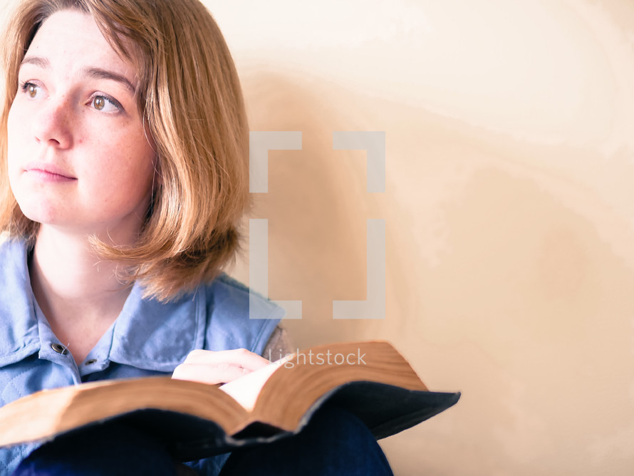a young woman reading a Bible and looking up to God 