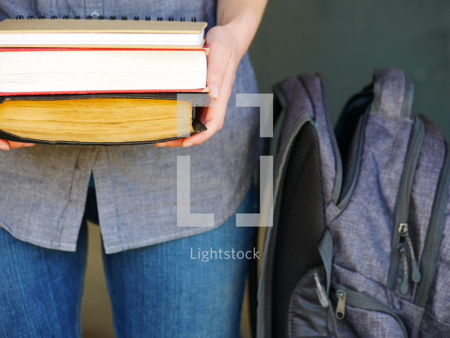 a student holding books near a book bag 