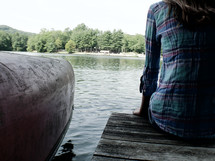 teen girl sitting on a pier on a lake beside a canoe 