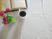 open Bible, vase of flowers, and coffee mug on a tablecloth 