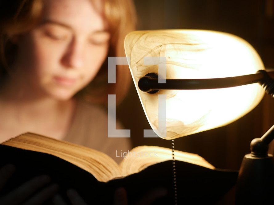 reading a Bible by the light of a desk lamp 