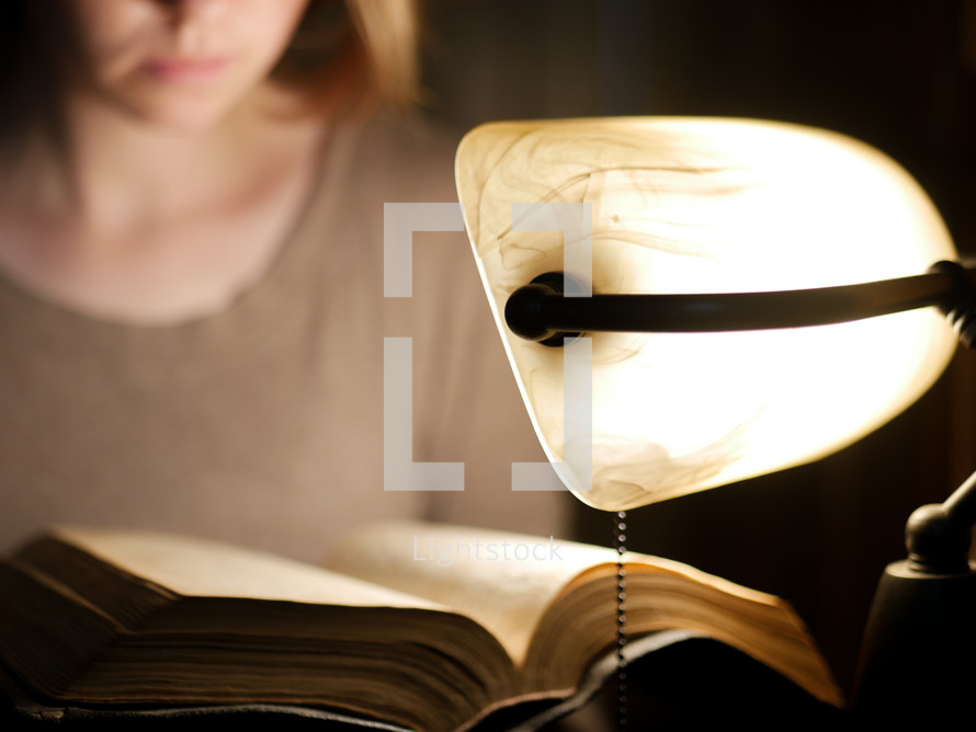 reading a Bible by the light of a desk lamp 