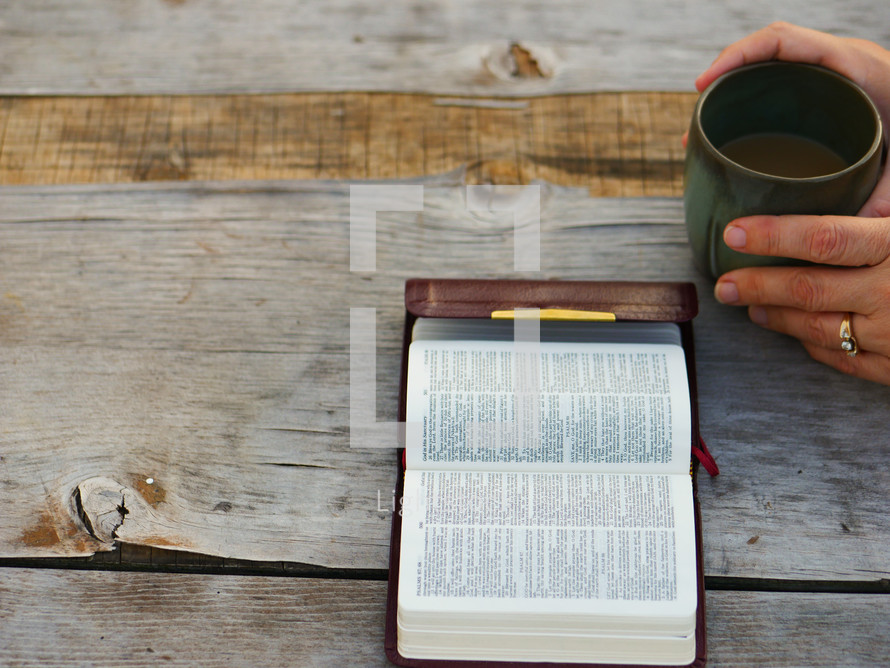 hand on a coffee mug while reading a pocket Bible 