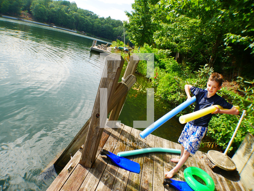 a boy child with pool noodles on a lake dock 