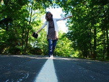 a teen girl walking on the center lines of a road holding a Bible 