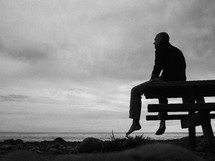 man sitting on a bench looking out at the ocean 