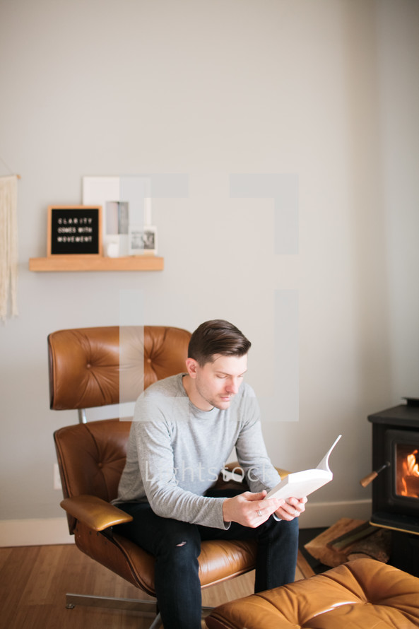 a man reading a Bible by a fireplace 