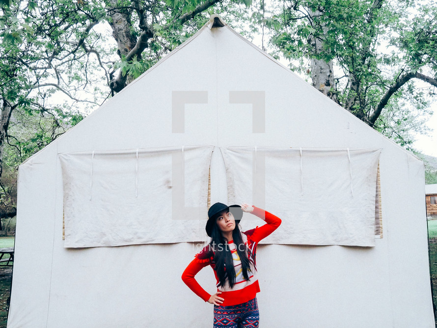Woman in a hat standing before a white canvas tent.