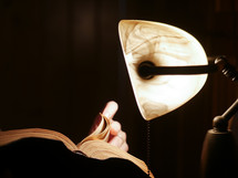 reading a Bible by light from a desk lamp 