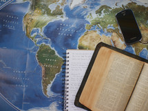 Bible, journal, and cellphone on a world map 