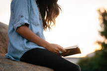 a woman sitting on a rock reading a Bible 