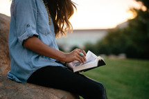 a woman sitting on a rock reading a Bible 