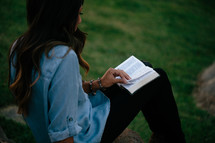 a woman sitting on a rock reading a Bible outdoors 