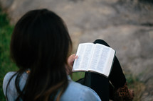 A woman sitting outside reading a Bible.