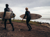 Surfers carrying surfboards along a beach.