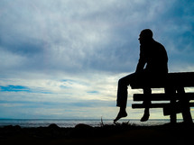 Silhouette of a man sitting on a pier looking out at the water.