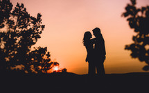 A silhouetted man and woman embracing at dusk. 