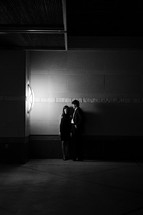 man and woman standing in front of a concrete wall at night