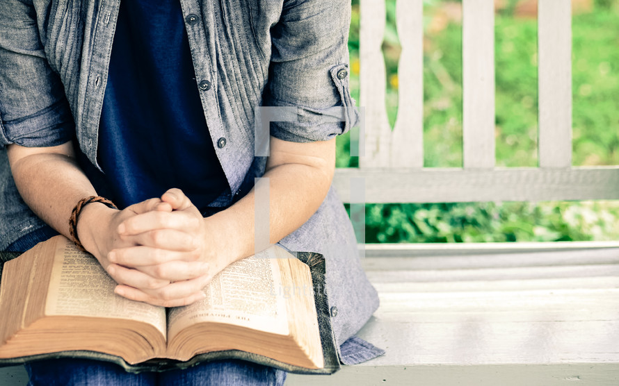 praying hands over a Bible while sitting on a bench 