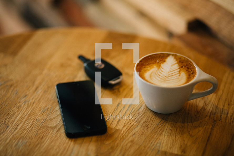 cellphone, car key, and coffee mug on a table 