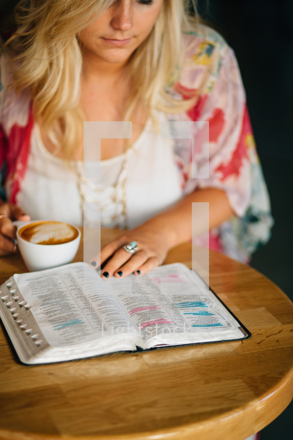A young woman reads a Bible, with a cup of coffee.