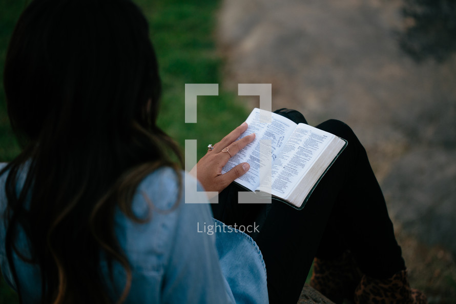 a woman sitting reading a Bible outdoors 