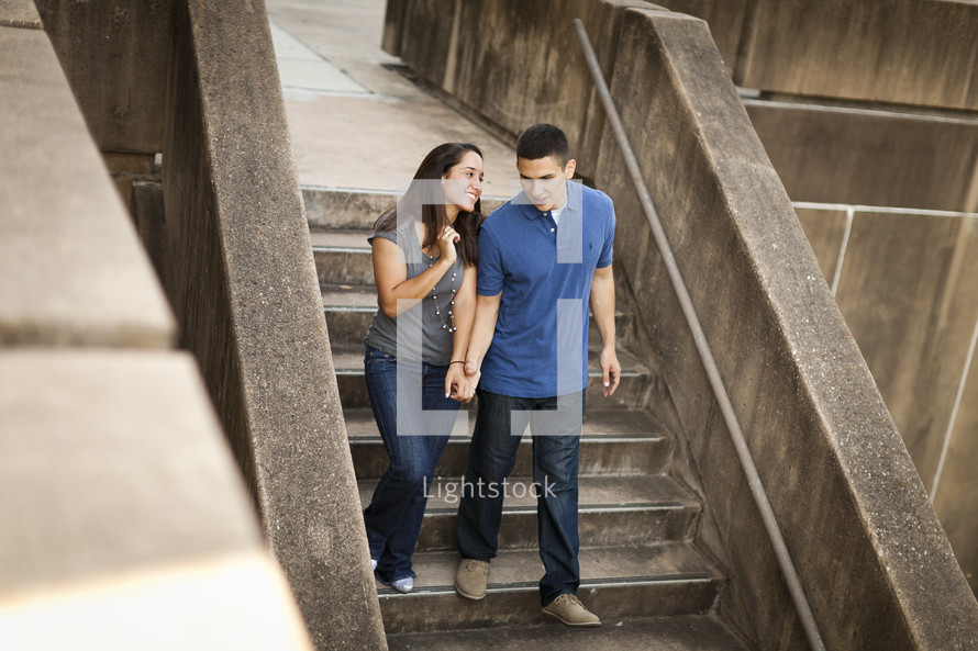 Couple in jeans holding hands while walking down cement steps.