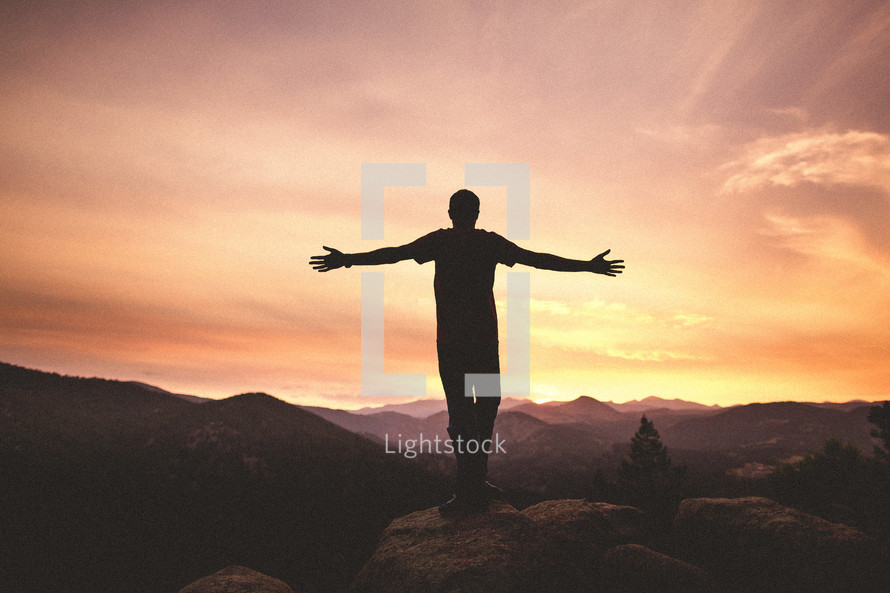 Man's arms raised at the top of mountain at sunset