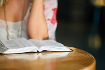 A young woman sits at a table with an open Bible.