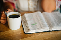 A young woman sits with a cup of coffee and an open Bible.