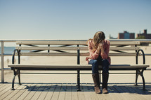 A young woman praying on a bench near Coney Island