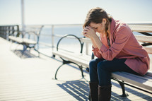 woman praying - sitting on  bench by ocean
