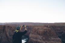 man taking a picture of a canyon with his cellphone 