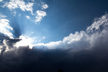Clouds move in to overtake the sun and cast rays of light from what looks like a glowing cloud formation. Darkness looms where the sun cannot penetrate. 