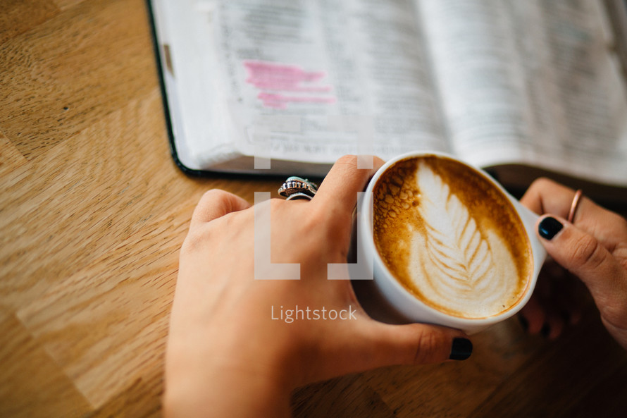 A woman holds a cup of latte' and reads the Bible.
