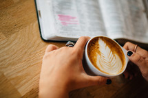 A woman holds a cup of latte' and reads the Bible.
