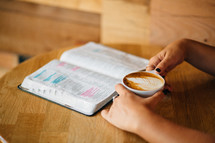 An open Bible and a cup of latte' held by a woman.
