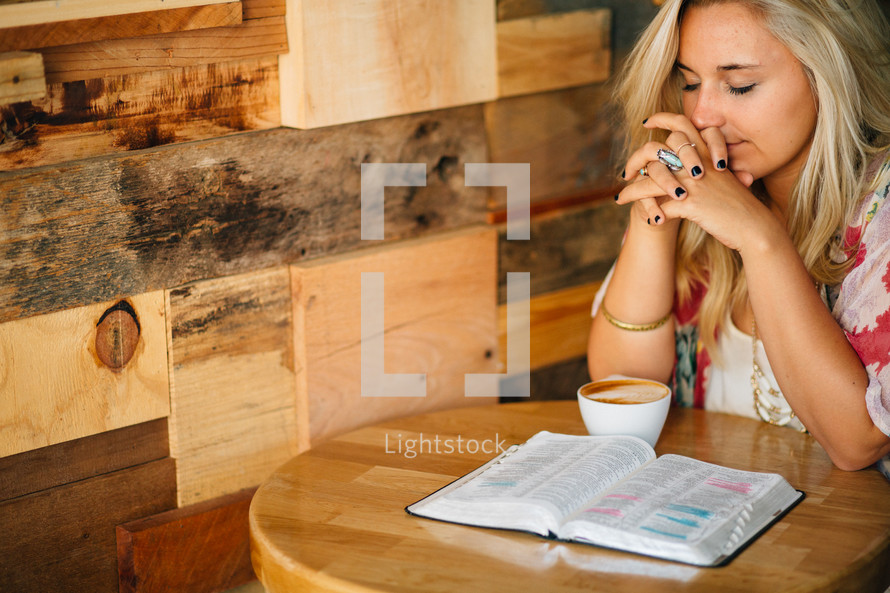 A young woman in prayer, with an open Bible and cup of coffee.
