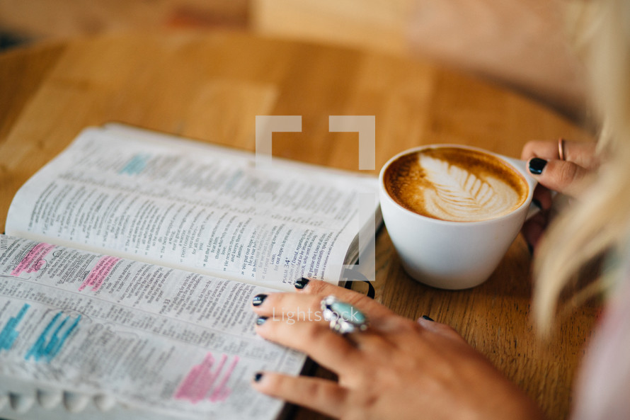 A woman reads a Bible and holds a cup of latte'.